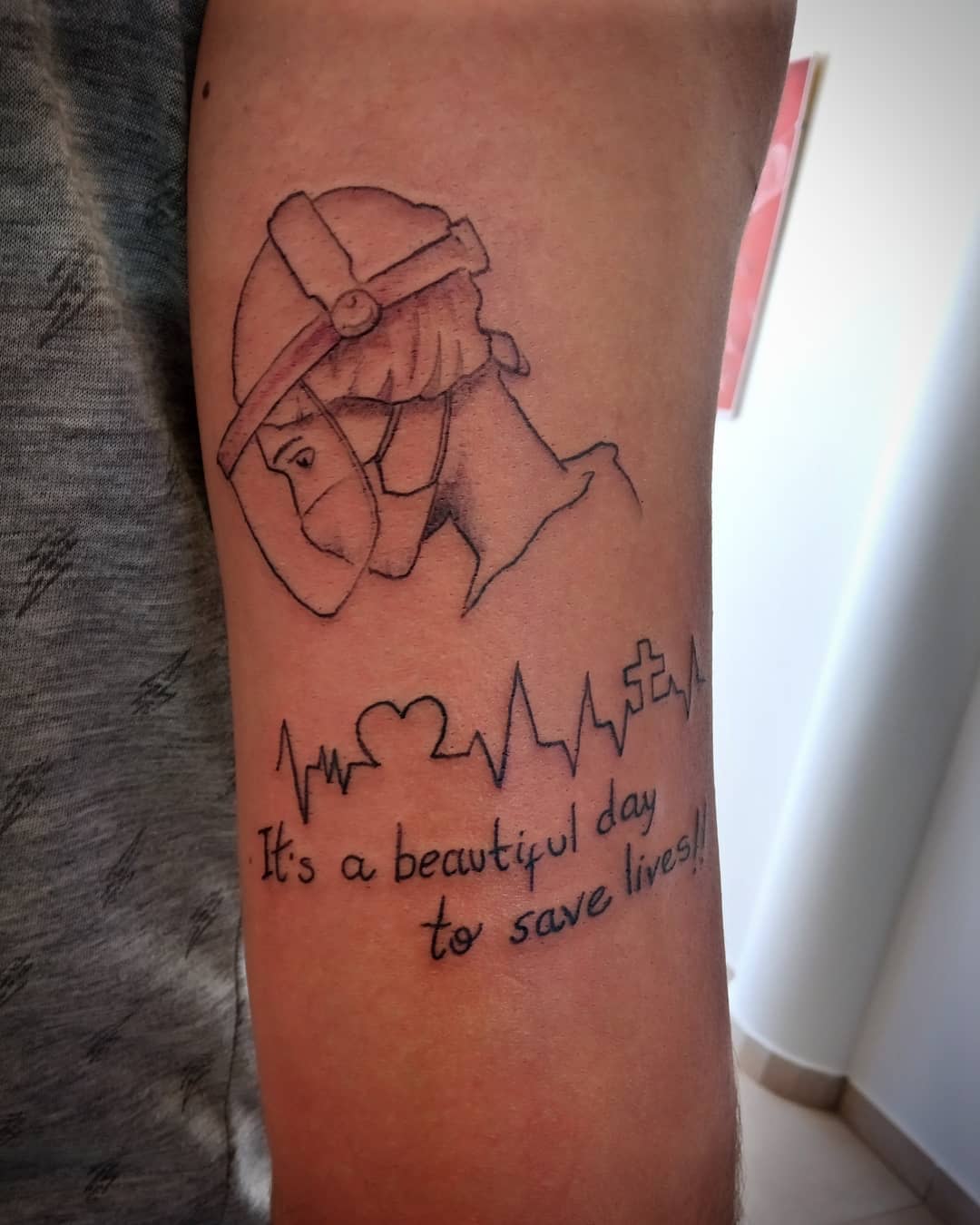 Tattoo of a masked nurse above an ECG line that reads "It's a beautiful day to save lives!"